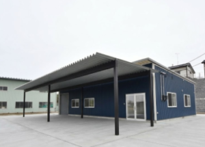 青いガルバリウム外壁と大きな折板屋根の庇が特徴的な水産加工場の外観全景